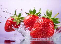 Three strawberries splashing into fresh water