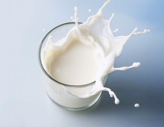 A glass of milk with the liquid splashing out of it.