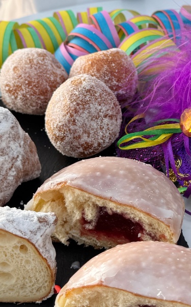 Colourful carneval pastries and candy with a purple and green carnival face mask next to it. 
