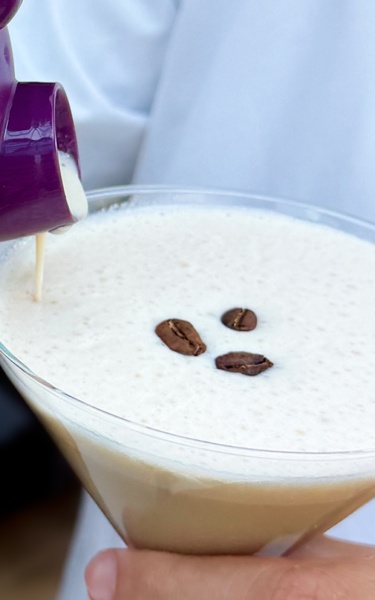 A cream coffee drink is poured into a martini glas from a purple OlrbichtArom shaker.