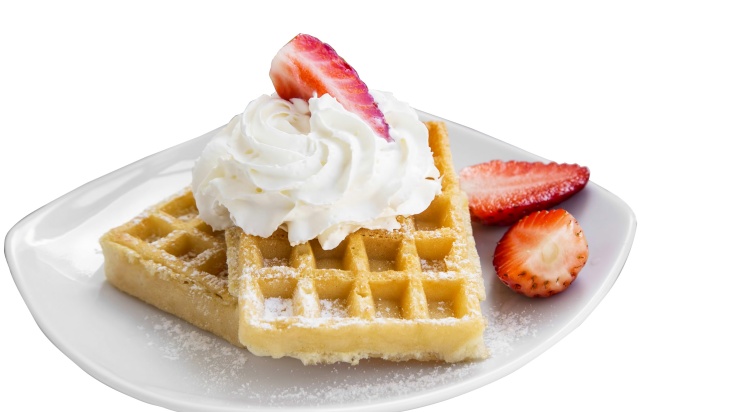 Two wafers on a white plate with delicious cream topping and strawberry pieces.