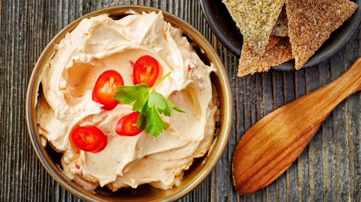 A bowl of reddish cream cheese with 4 cherry tomatoes and a piece of parsley on top.