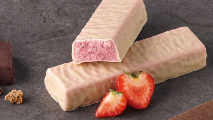 Two strawberry protein sports bars covered in white chocolate with pieces of strawberry next to it.