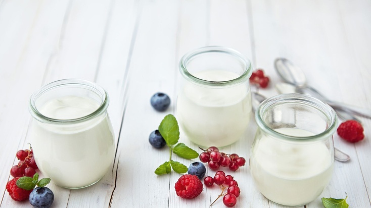 three glasses of natural yoghurt with some red berries as decoration around them.