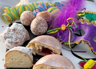 Colourful carneval pastries and candy with a purple and green carnival face mask next to it. 