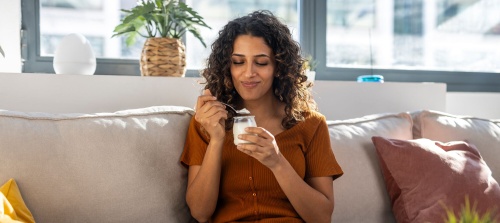 Young woman sitting on the couch, enjoying a joghurt